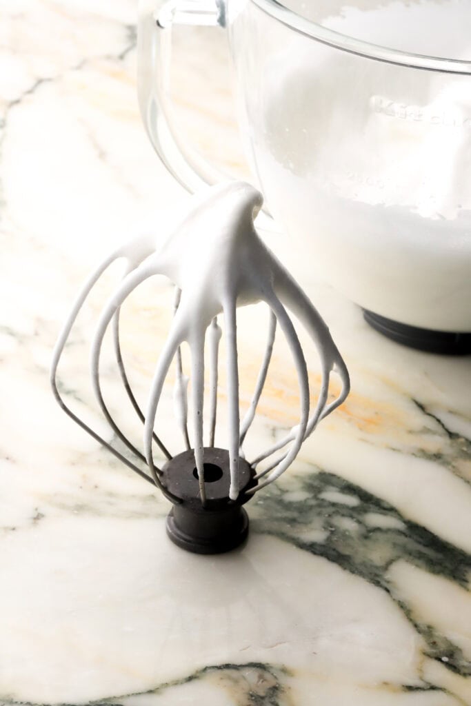 meringue at stiff peaks on a whisk with the bowl behind