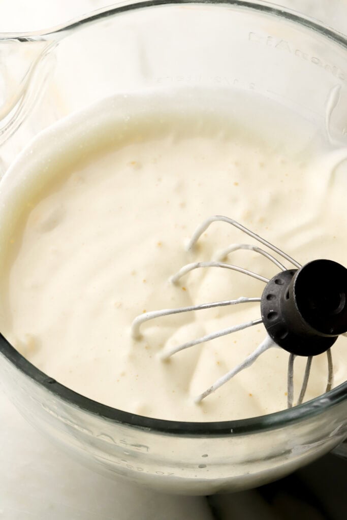 cake batter halfway done in a glass mixer bowl with the whisk attachment