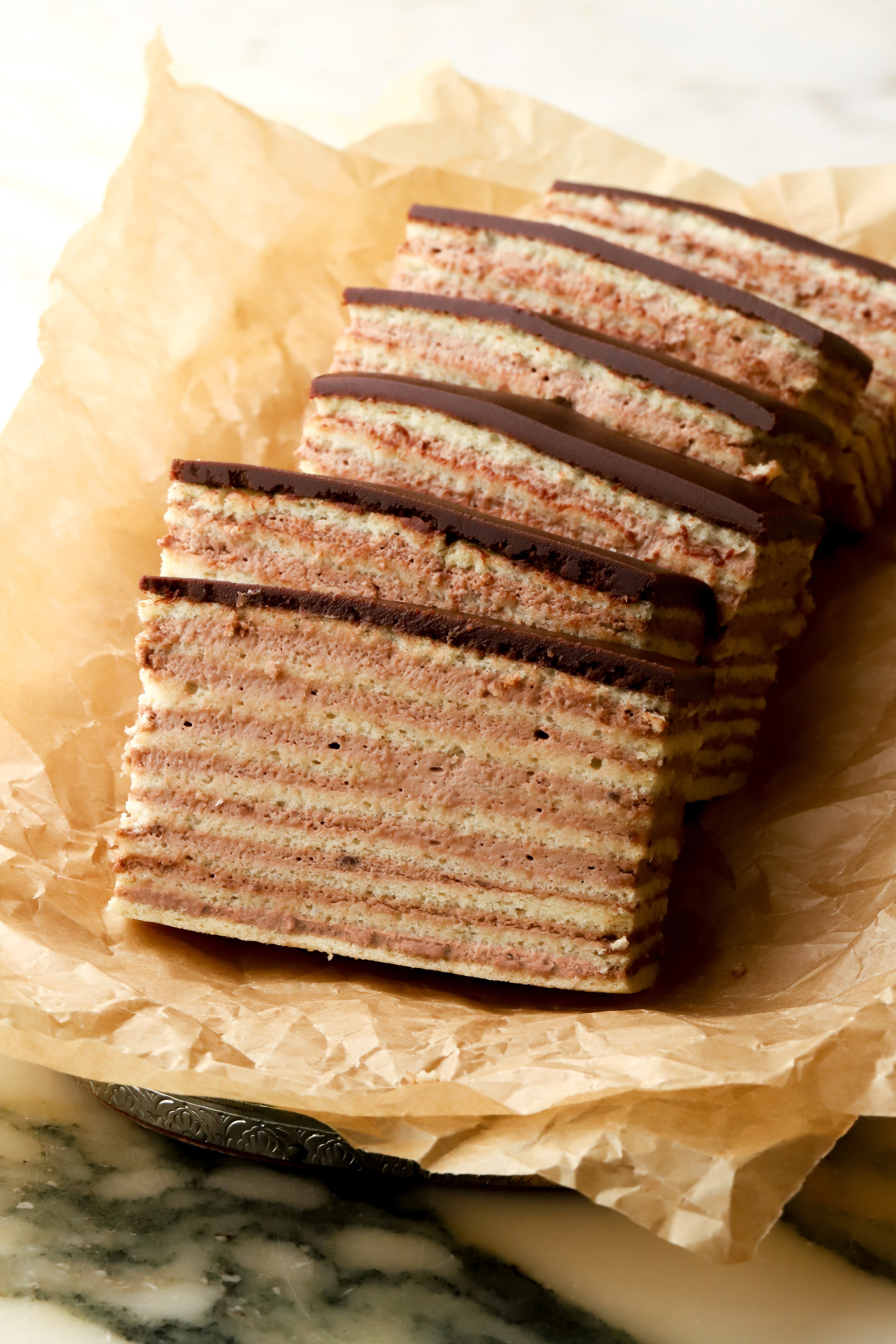 6 slices of dobos on a tray with brown parchment paper - sliced showing all the layers of cake