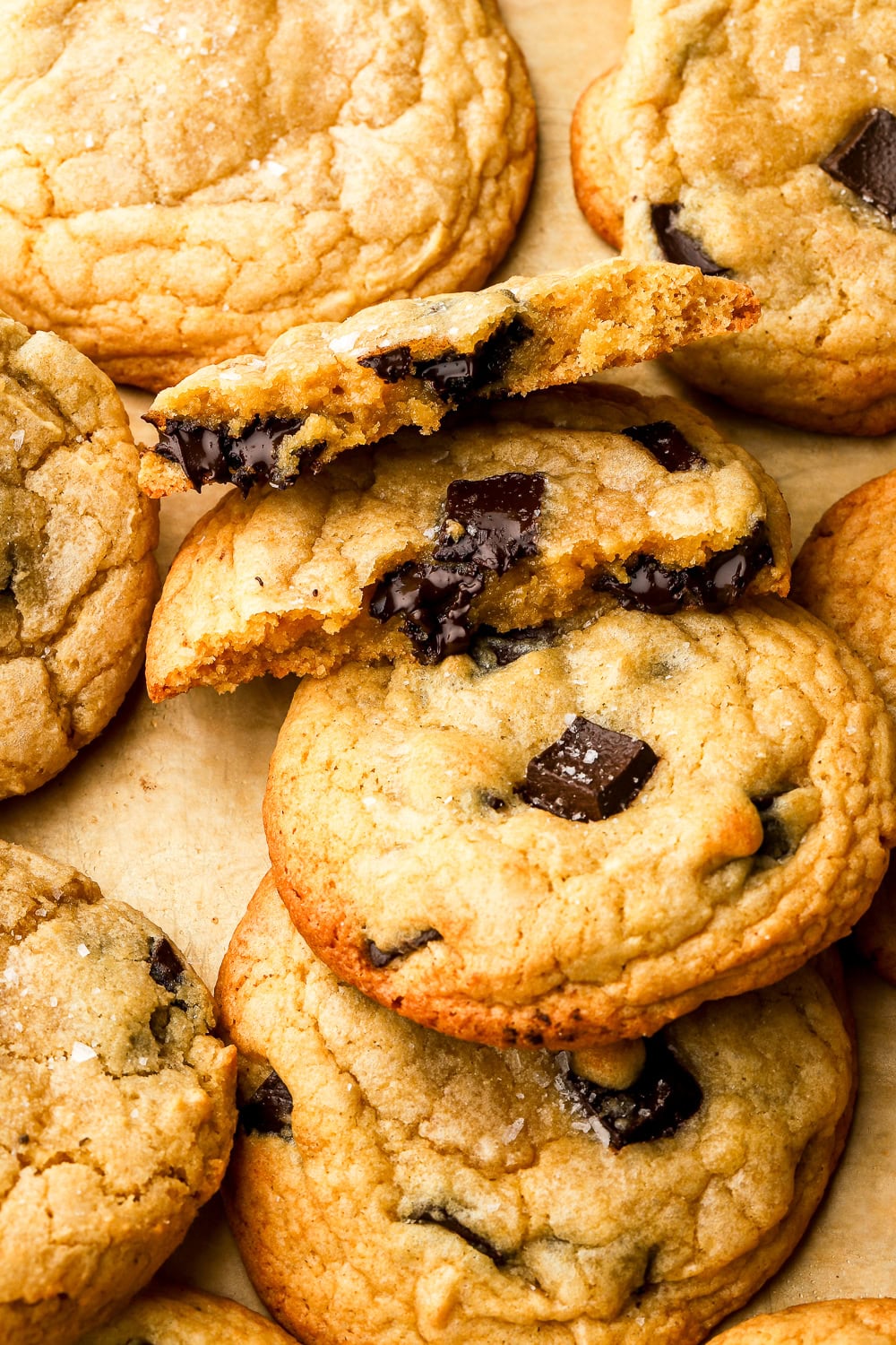 pile of chocolate chip cookies on top of one another on a sheet pan. one broken in half to show inside