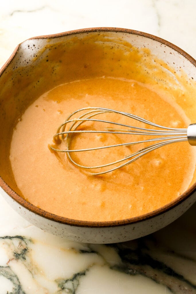 eggs whisked into batter in a pottery bowl with a whisk