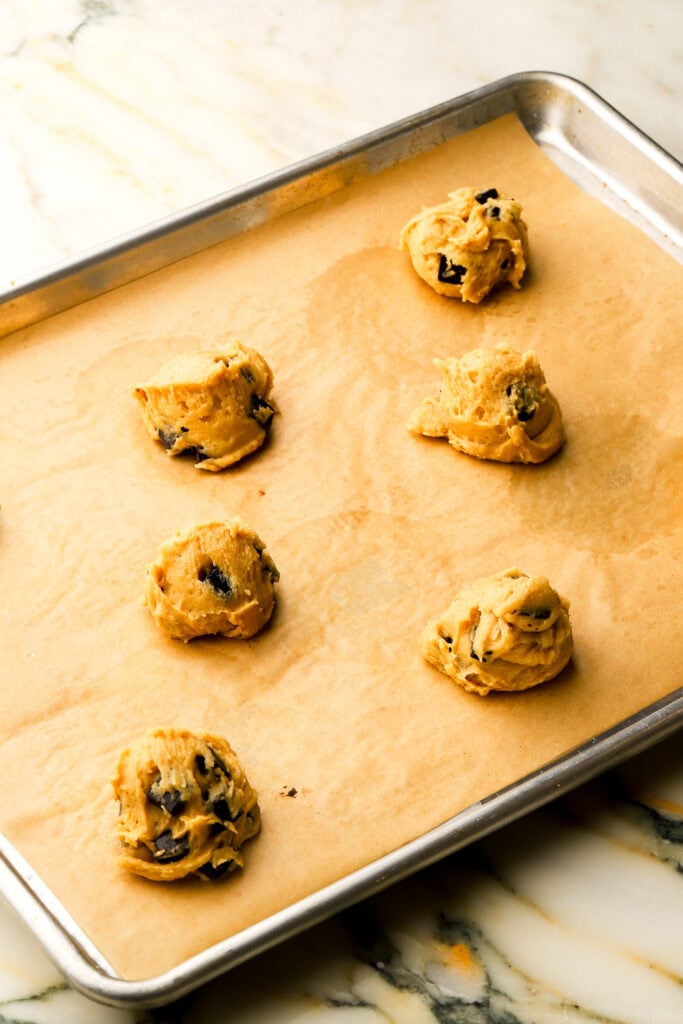 cookie dough scoops two inches apart on a cookie sheet lined with brown parchment paper