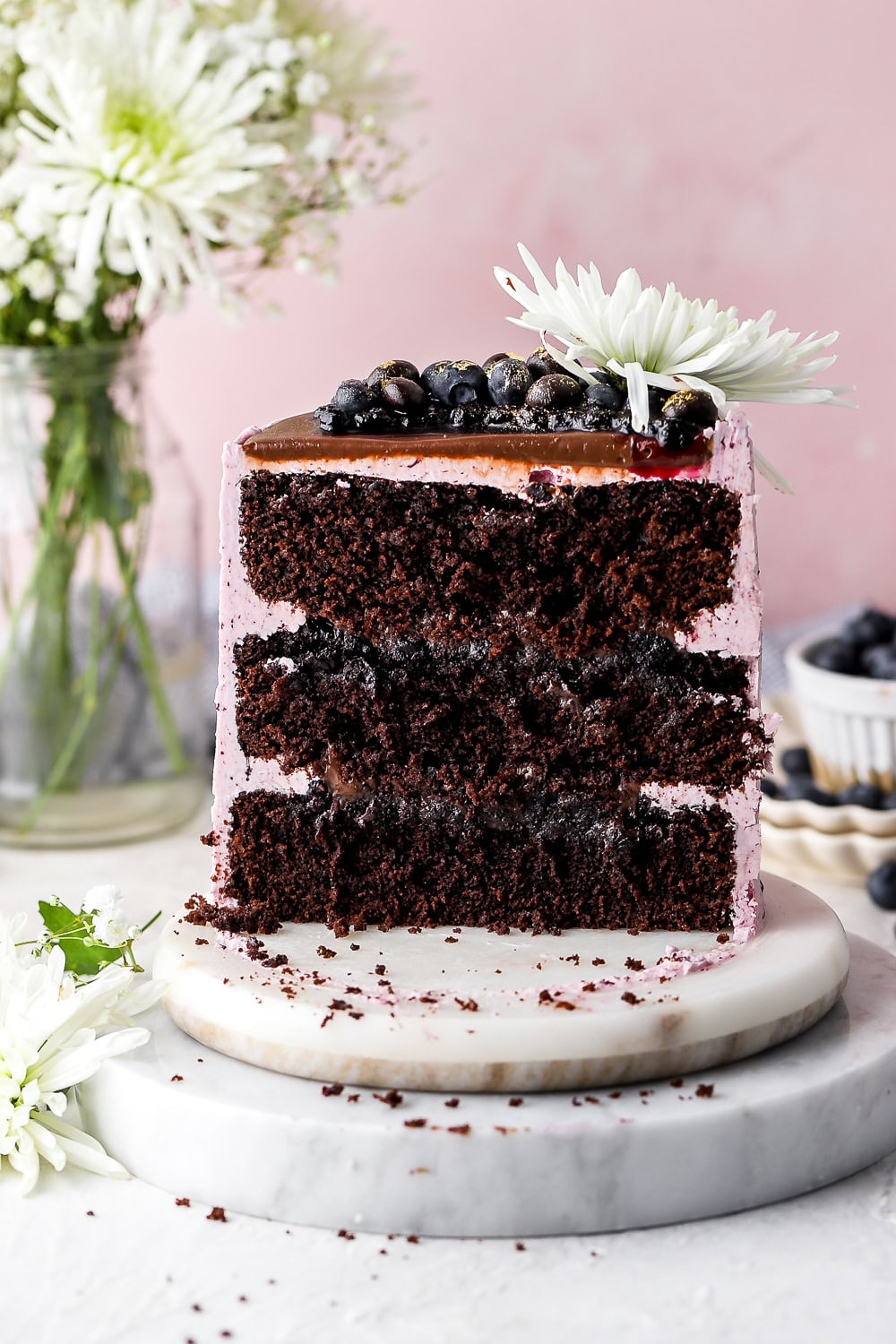 blueberry chocolate cake sliced in half on a marble tray with flowers in the background