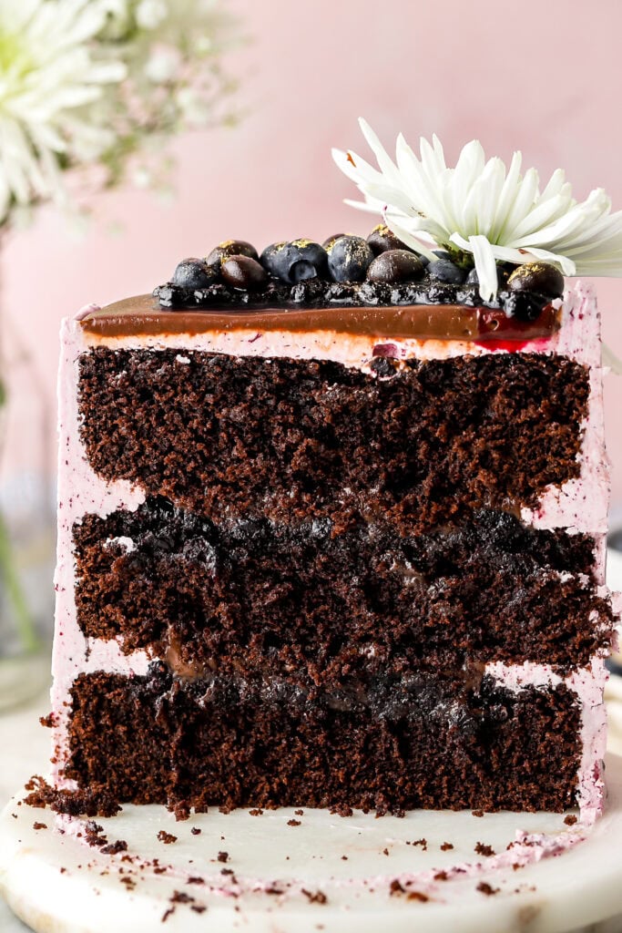 blueberry chocolate cake sliced in half on a marble tray with flowers in the background