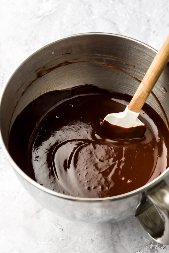 Melted chocolate ganache in a mixer bowl with a spatula