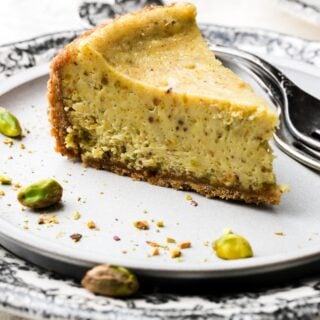 slice of pistachio cheesecake on a plate with pistachios on the side