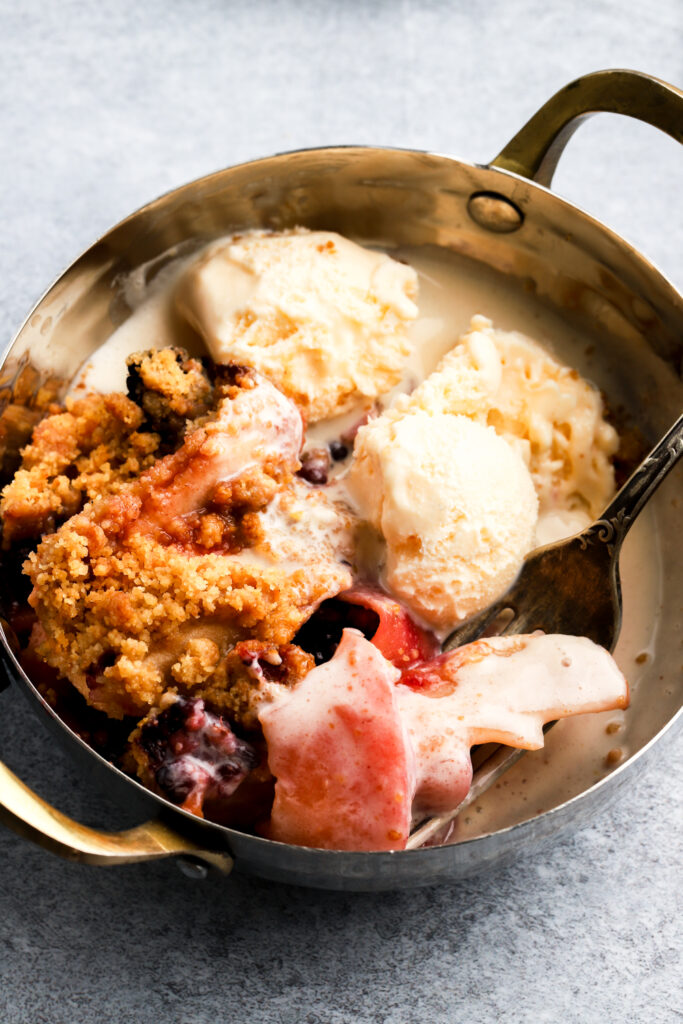 apple blackberry crumble with melting ice cream in bowl