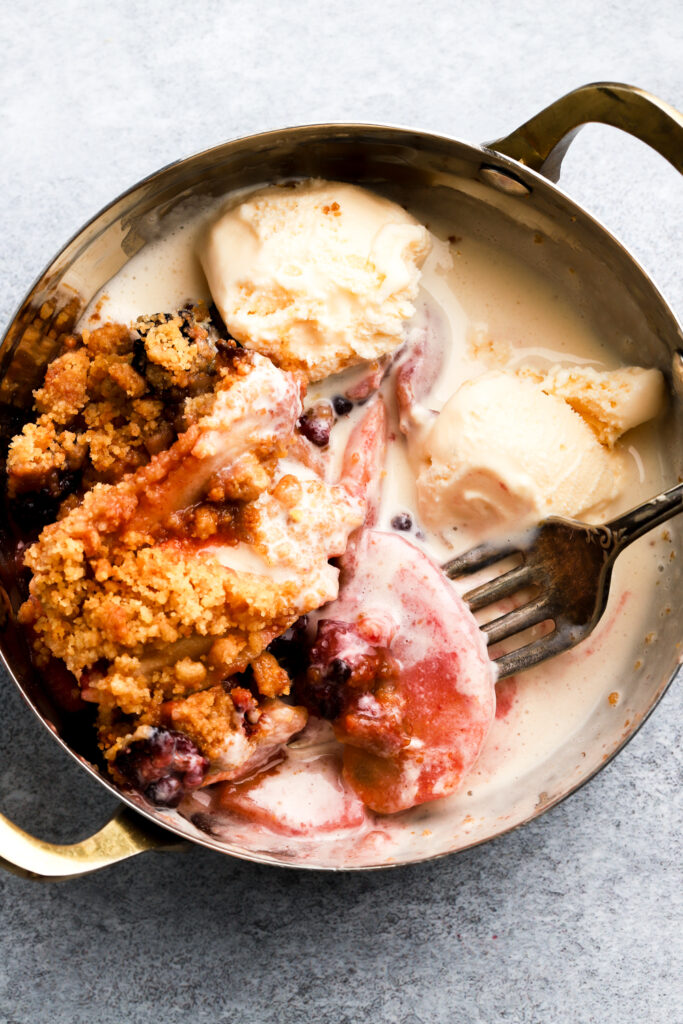 apple blackberry crumble in a bowl with melting ice cream