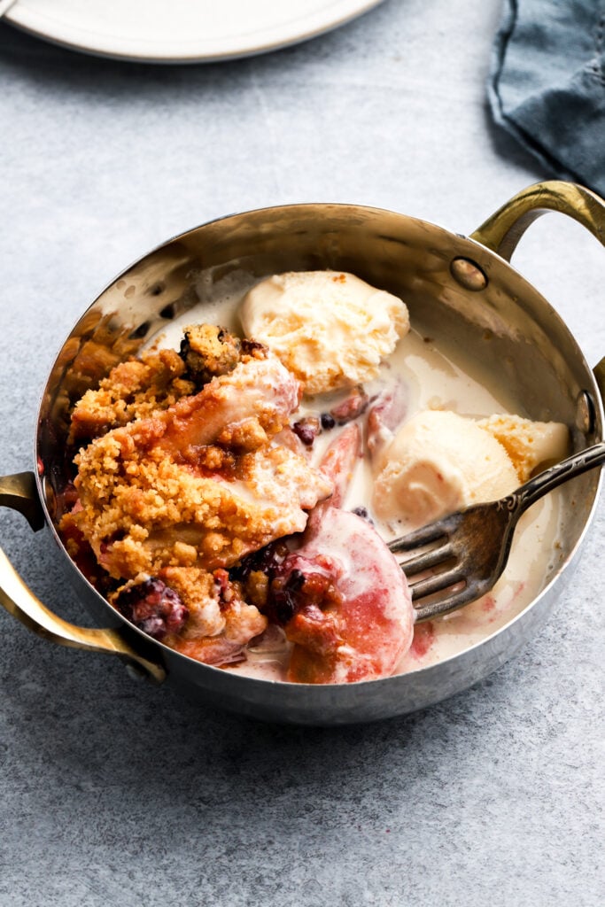 apple blackberry crumble in a bowl with ice cream and a fork