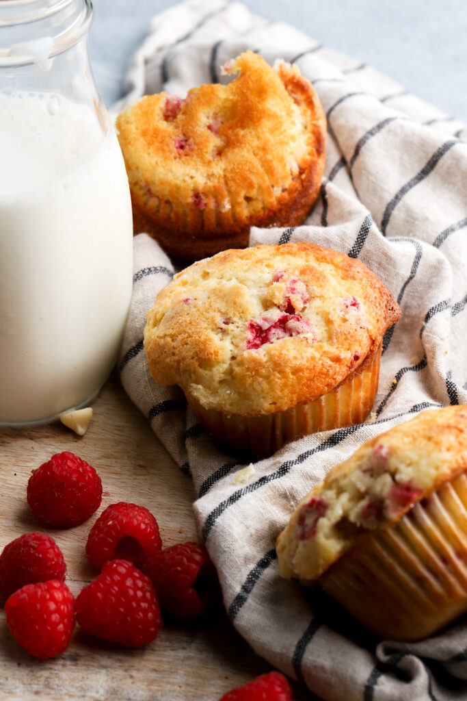 muffins sitting next a glass of milk and raspberries