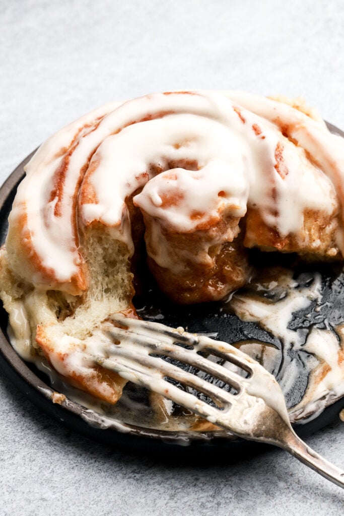 cinnamon roll on a plate and half eaten with a fork