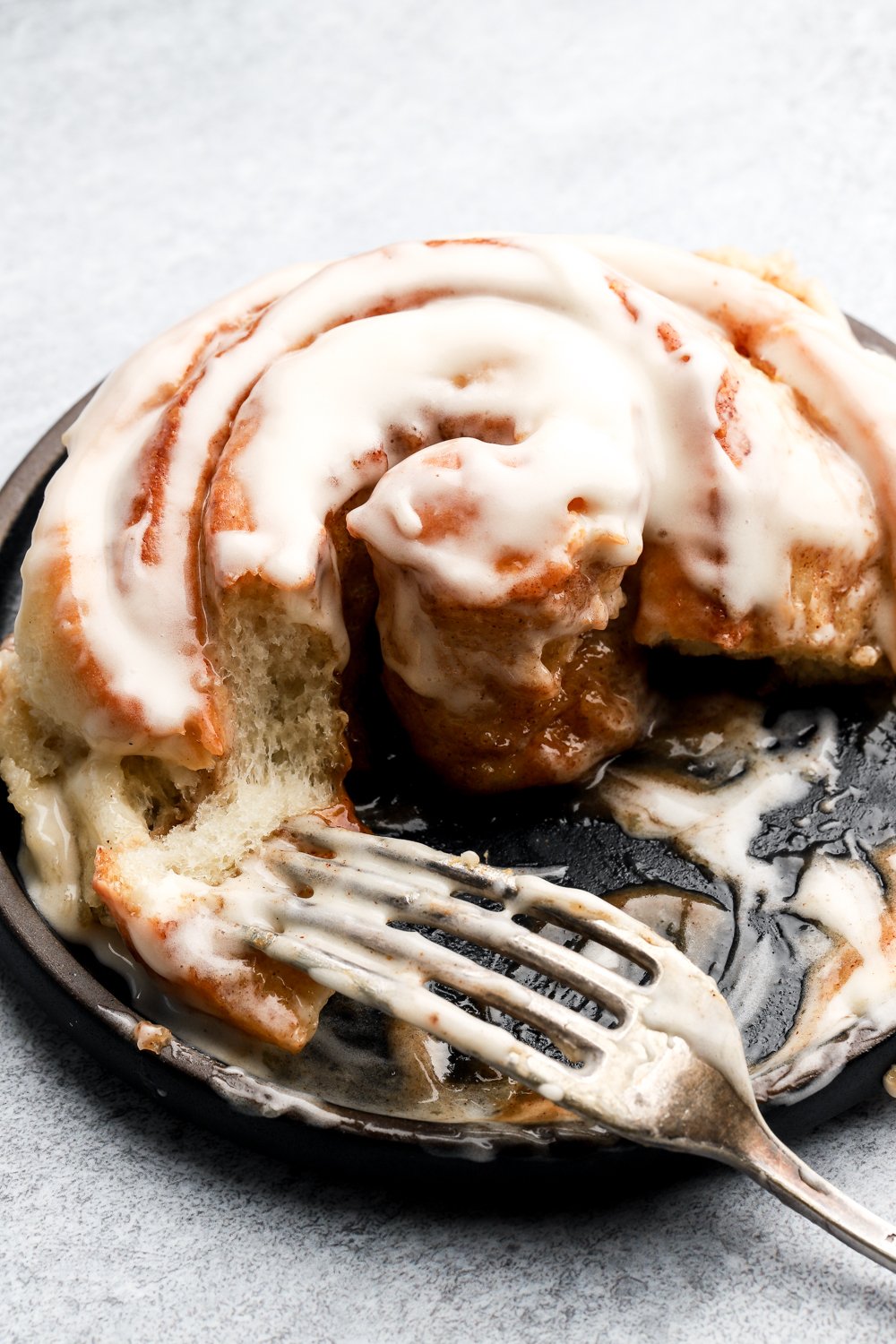 cinnamon roll on a plate and half eaten with a fork