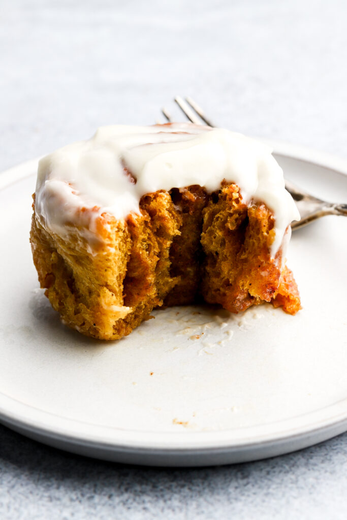 pumpkin cinnamon rolls with cream cheese frosting on a plate with a bite taken out