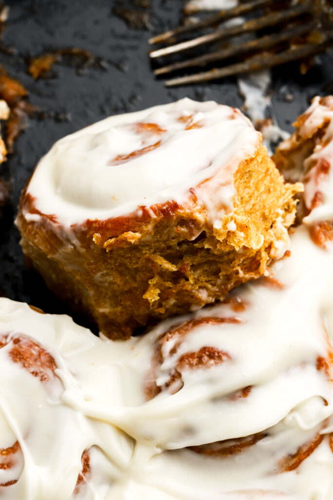 pumpkin cinnamon roll slightly raised above other rolls still in the pan with a fork above it