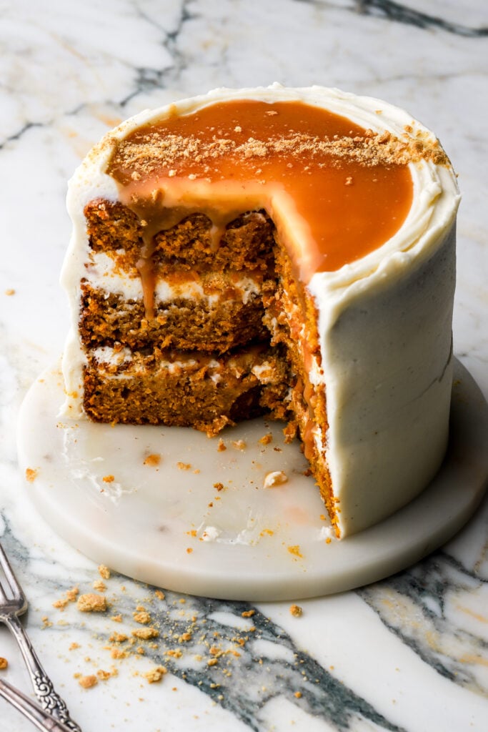 Pumpkin cake frosted with cream cheese frosting and topped with salted caramel sauce, partly cut in to 