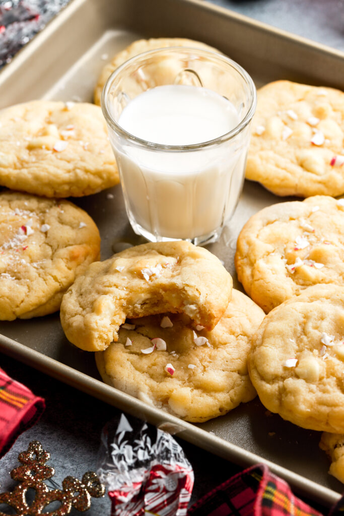 white chocolate peppermint cookies on a tray with a bite taken out and a glass of milk
