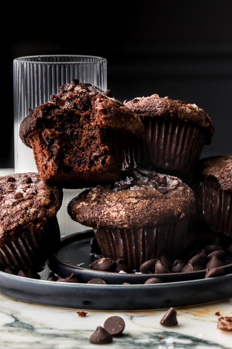 Chocolate muffins stacked next to a glass of milk and a bite taken out of the muffin