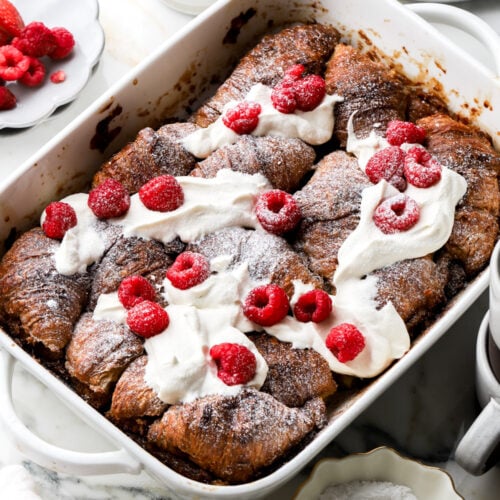 croissant french toast casserole topped with whipped cream and raspberries