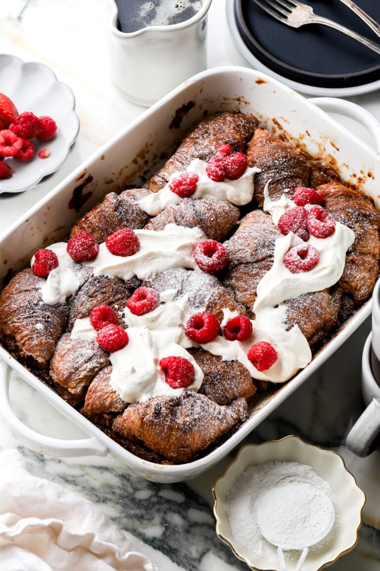 croissant french toast casserole topped with whipped cream and raspberries