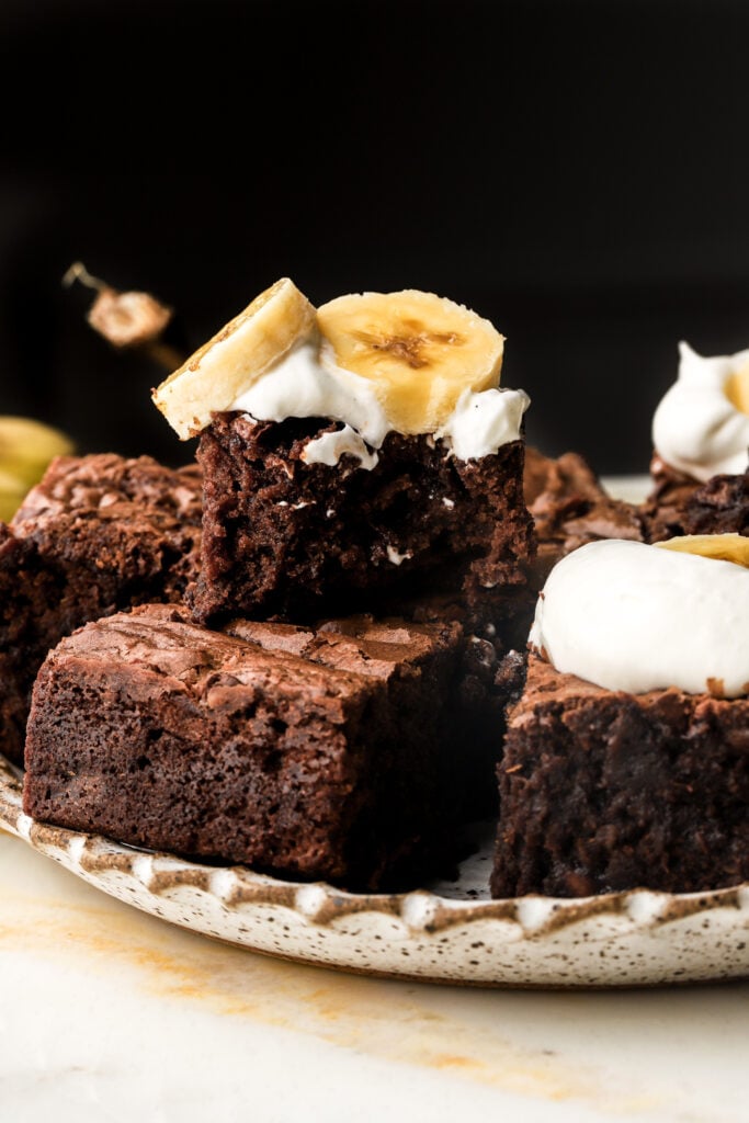 banana brownies stacked and topped with whipped cream and banana slices