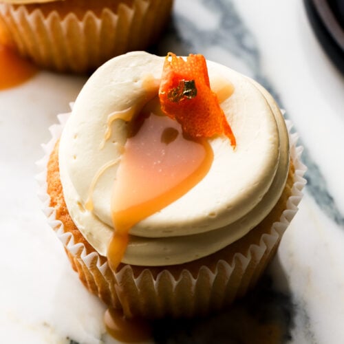orange cupcakes topped with orange buttercream, orange caramel sauce and a slice of orange peel