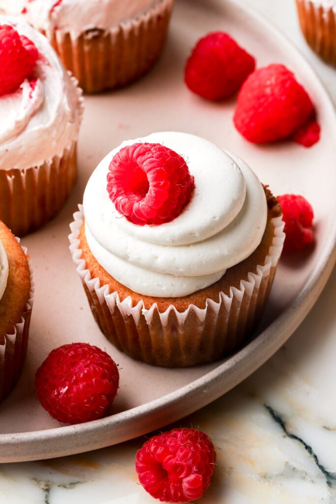 cupcakes frosted with white chocolate buttercream and topped with raspberries 