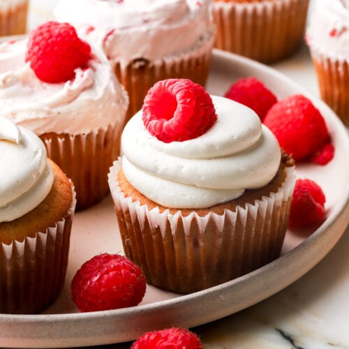 white chocolate raspberry cupcakes on a plate with raspberries
