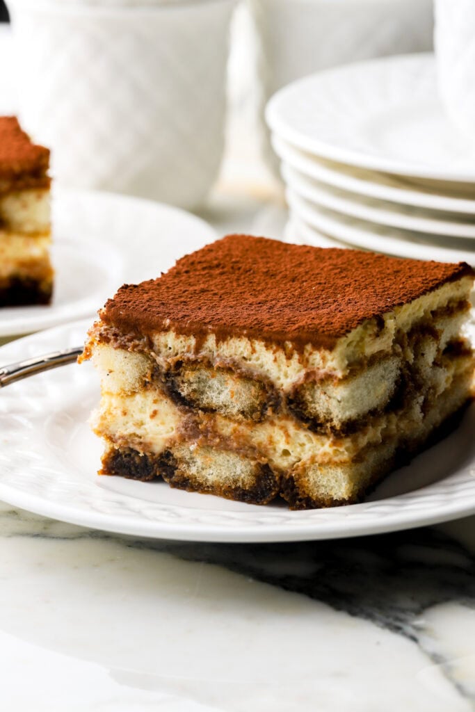 slice of Tiramisu on a plate with plates in the background