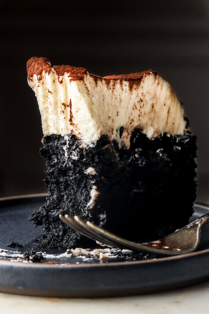 slice of black cocoa cake on a plate frosted with mascarpone cream