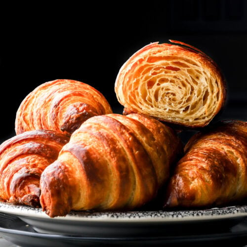 fresh homemade croissants on a plate with one cut in half to show the inside