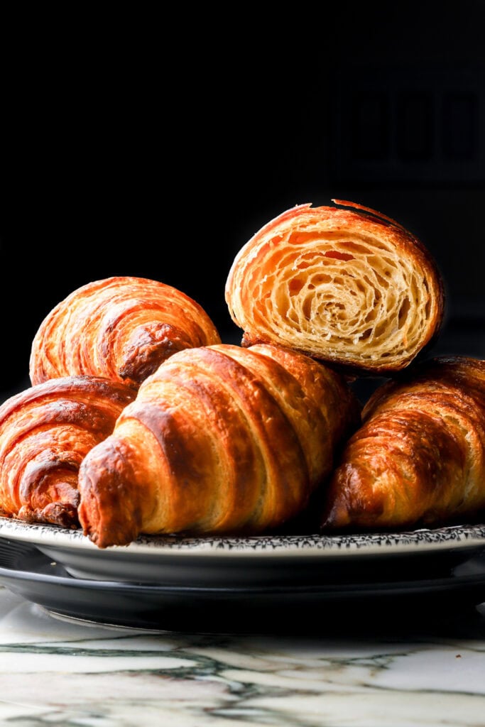 fresh homemade croissants on a plate with one cut in half to show the inside