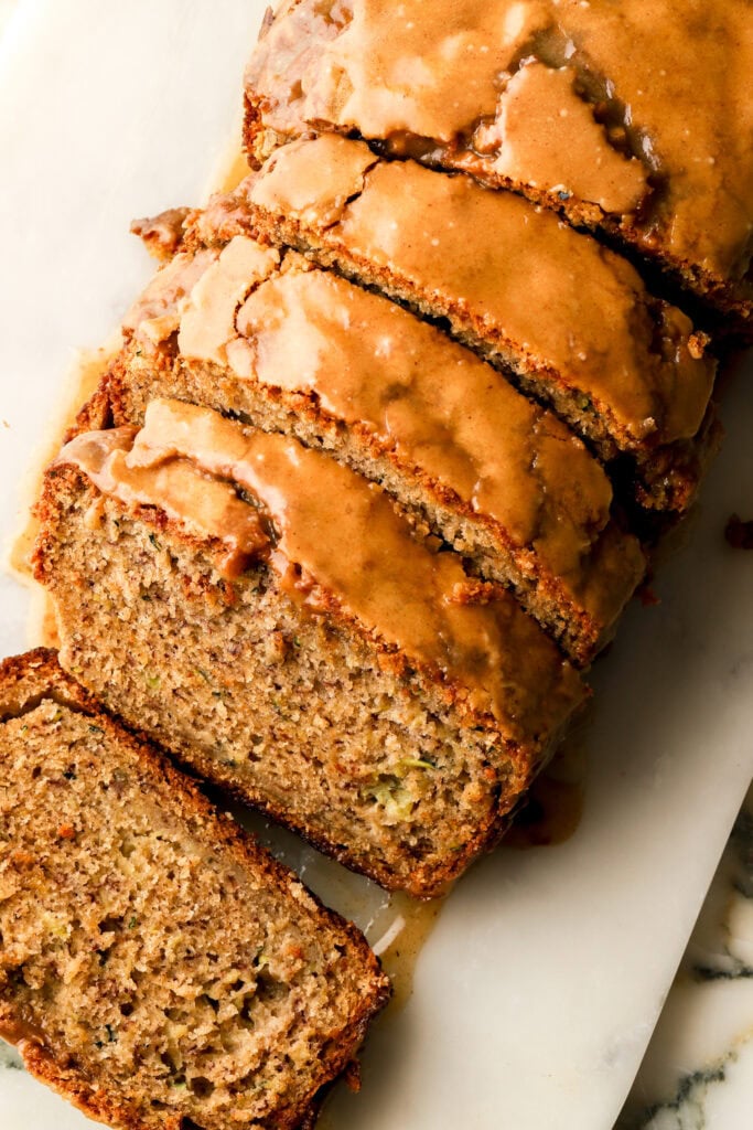 close up of zucchini banana bread with brown sugar glaze, sliced on a cutting board