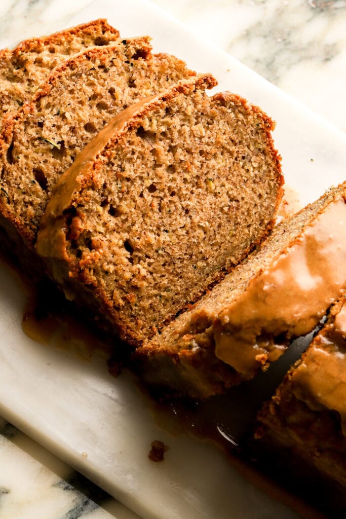 banana zucchini bread with brown sugar glaze, sliced on a cutting board