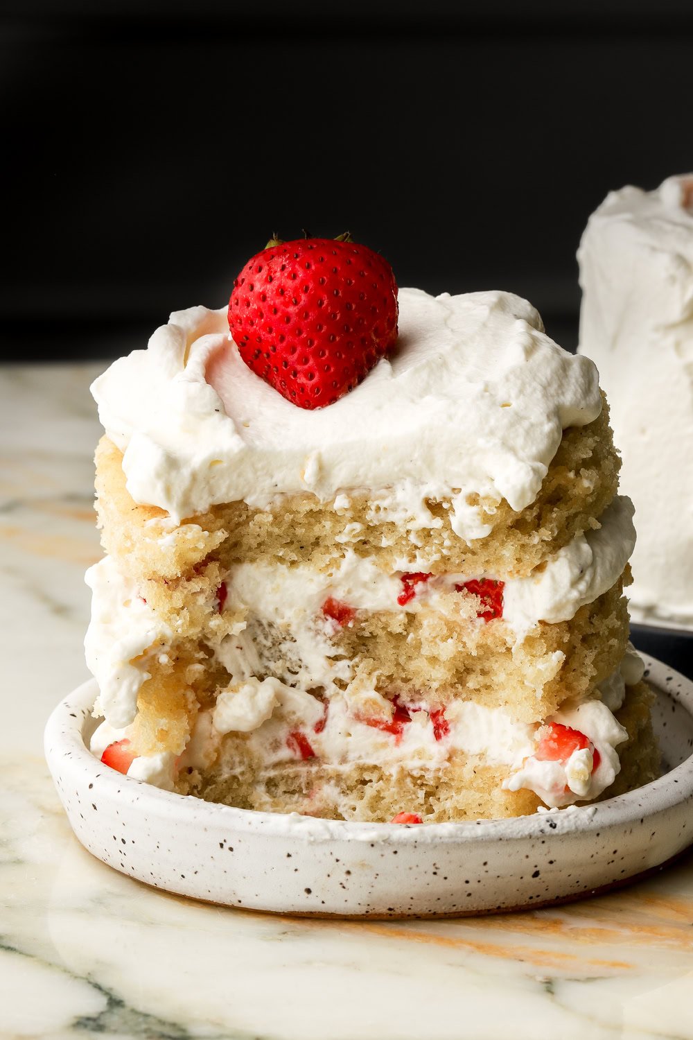 mini vanilla cake layered with whipped cream and strawberry chunks with a bite taken out of the cake