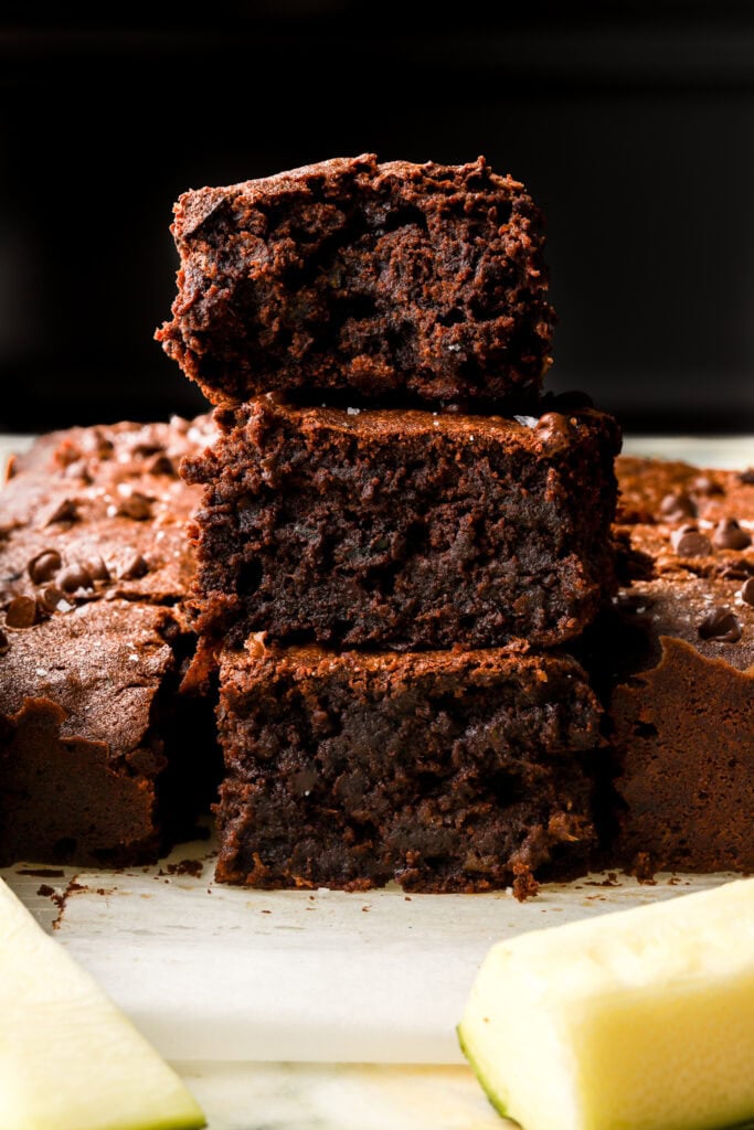 Stack of three zucchini brownies with a sliced zucchini next to it