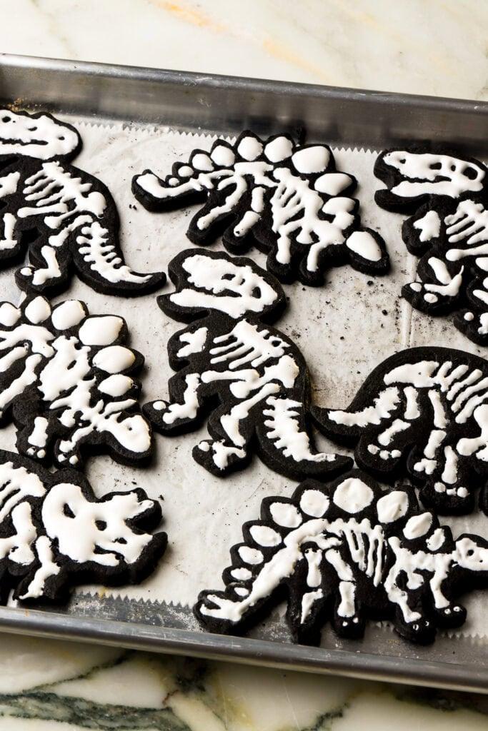 black cocoa sugar cookie cut into the shape of dinosaur and icing piped as bones