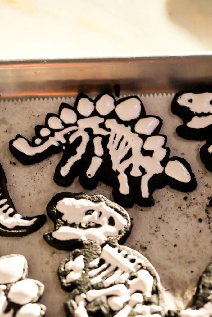 black cocoa sugar cookie cut into the shape of dinosaur and icing piped as bones