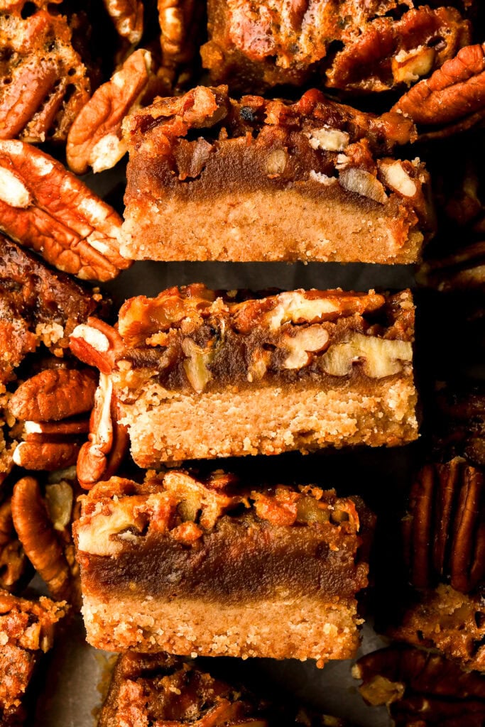 close up of three slices of pecan pie bars surrounded by pecans