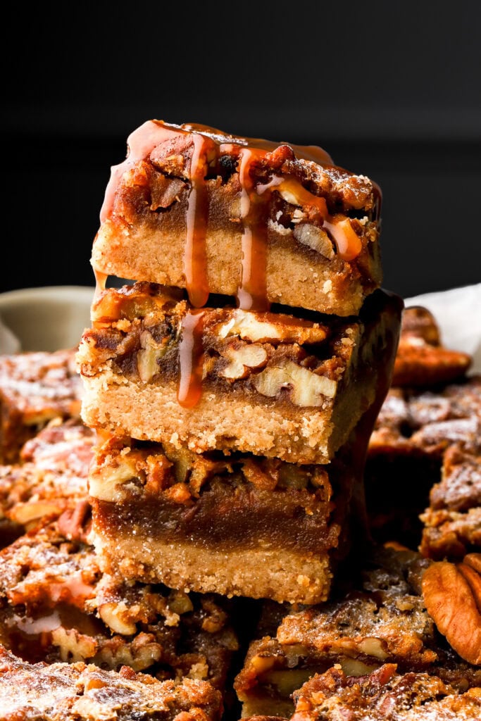 pecan pie bars stacked and topped with salted caramel sauce