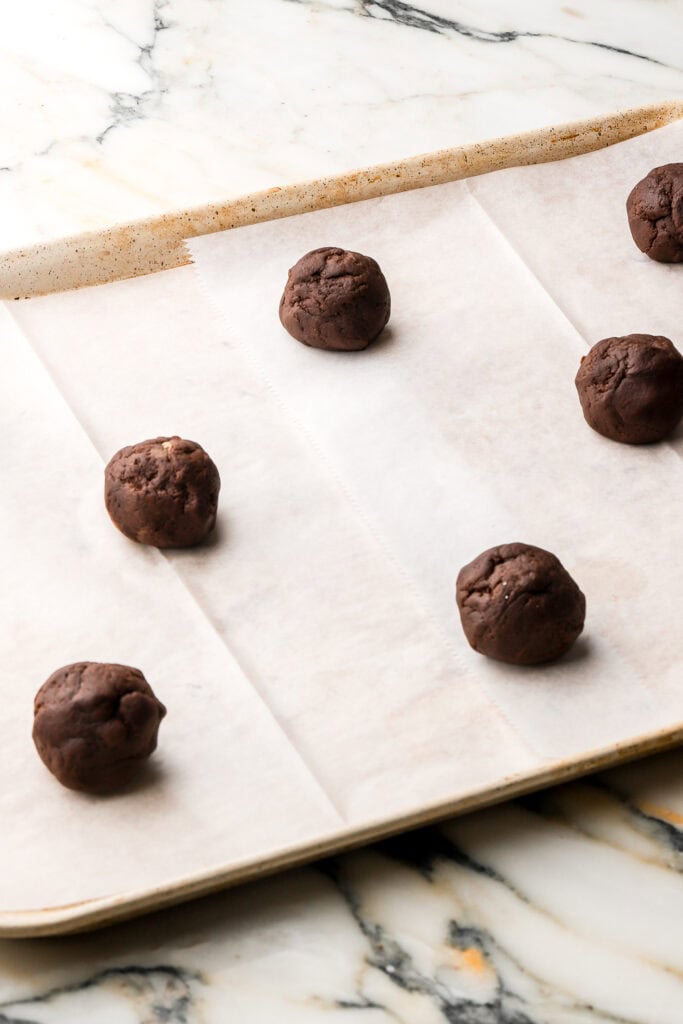 chocolate cookie dough balls rolled out on cookie sheet