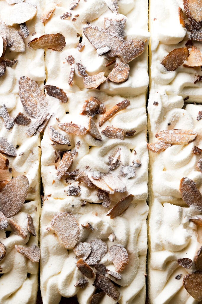 close up of topping on almond croissant cake with piped chantilly cream, toasted almonds, and powdered sugar
