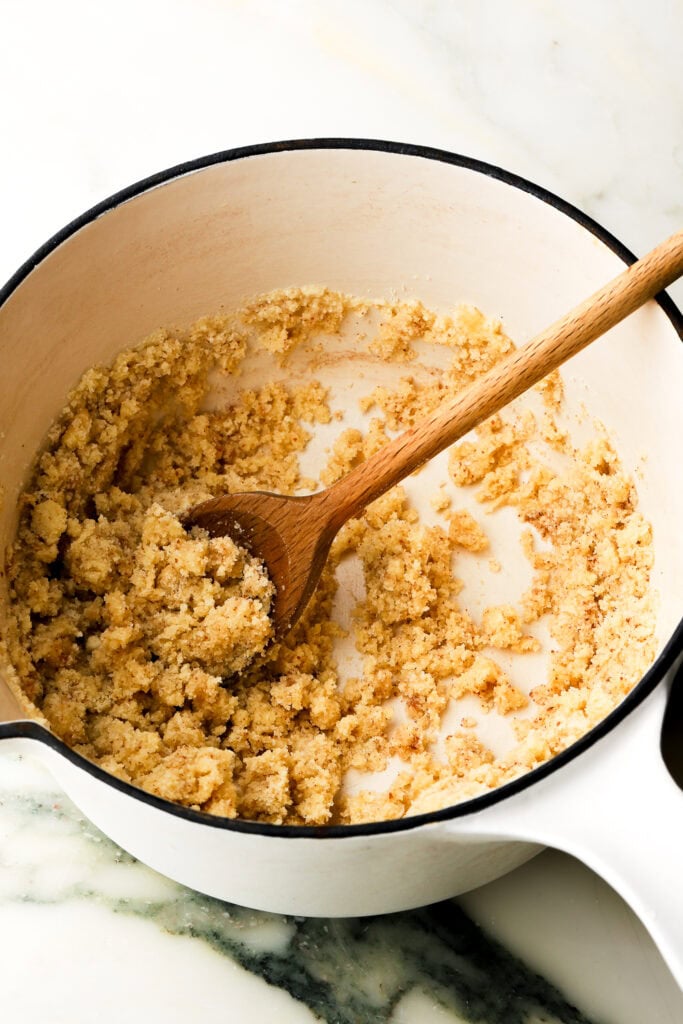 flour and almond flour mixed with brown butter in saucepan and wooden spoon mixing them
