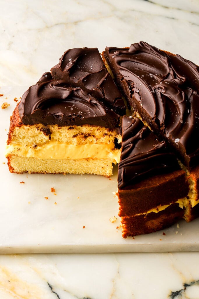 Boston cream pie cake on a marble slab on a marble counter, sliced showing the inside