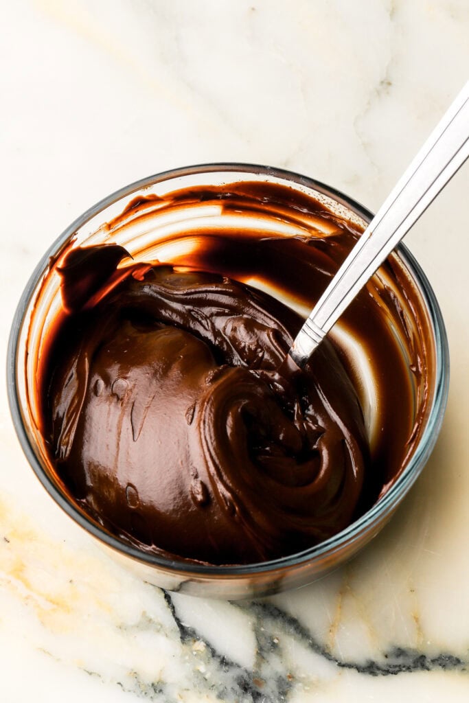 dark chocolate ganache cooled and spreadable in a bowl with a spoon