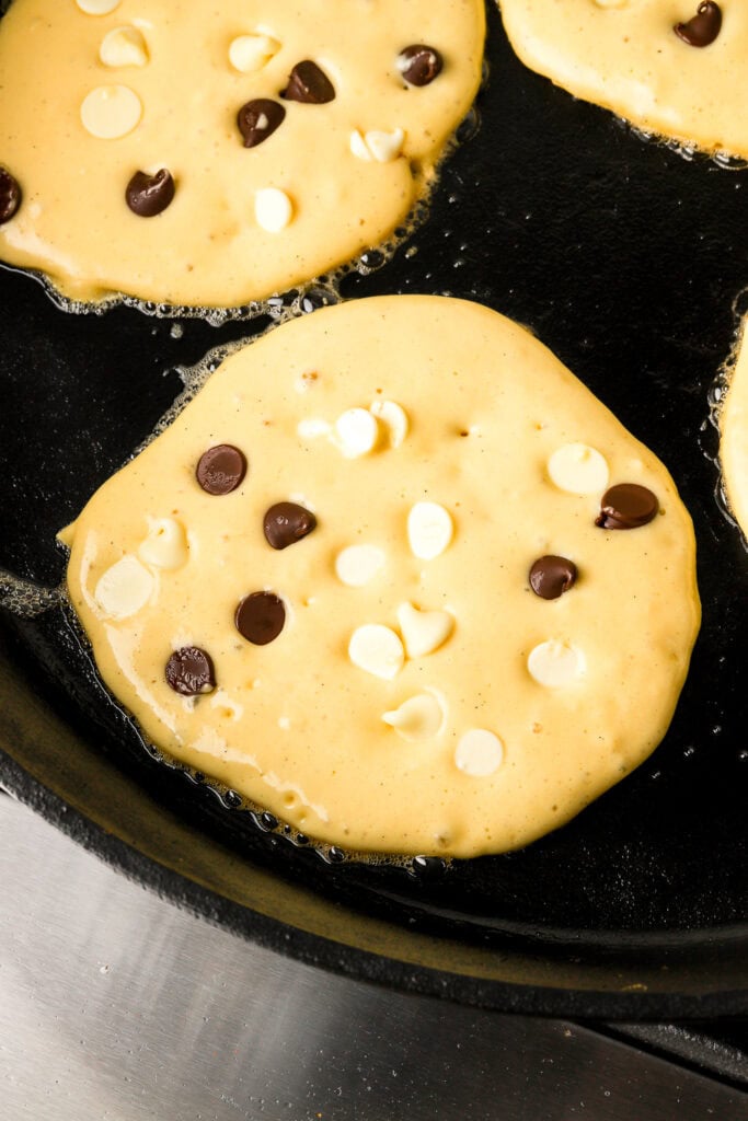 cottage cheese pancakes cooking on a cast iron with white chocolate and dark chocolate chips