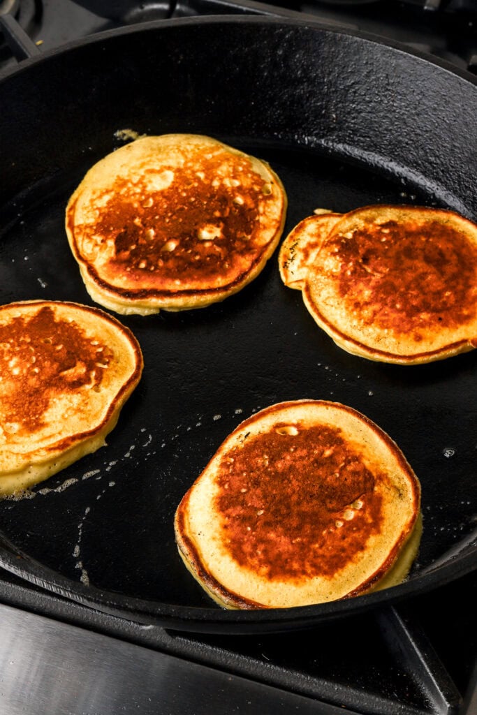 4 pancakes cooking on cast iron before flipping