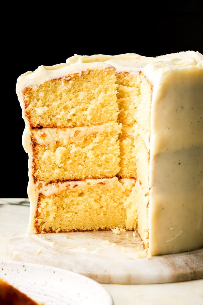 three layer vanilla cake with vanilla buttercream sliced and standing tall showing the inside of the cake
