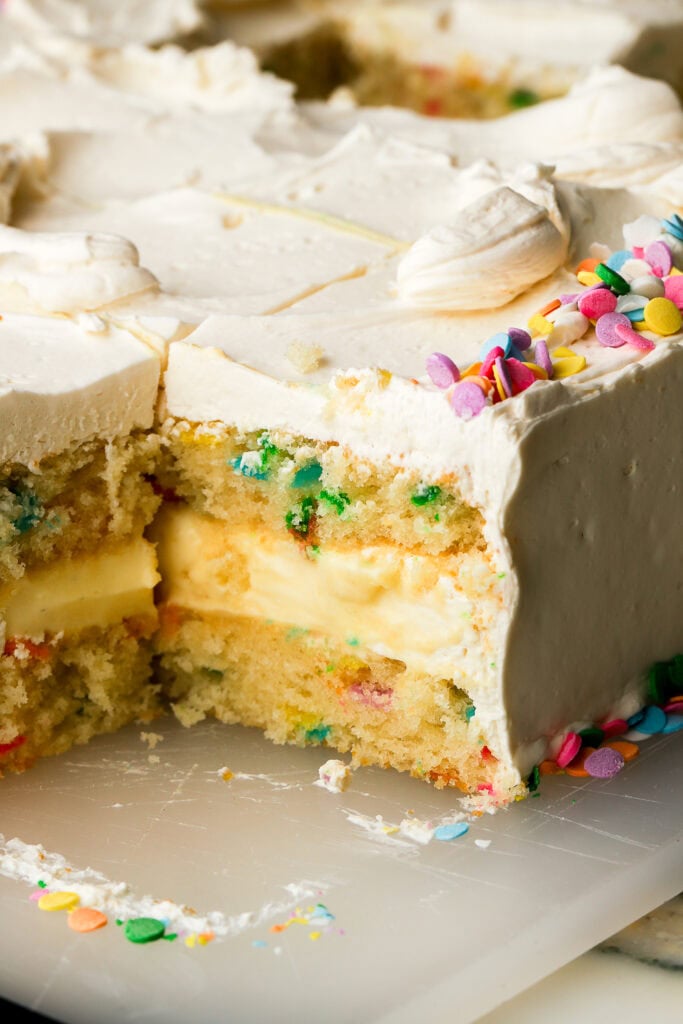 close up of a slice of vanilla cake with custard filling and sprinkles, sliced on the cutting board, corner piece