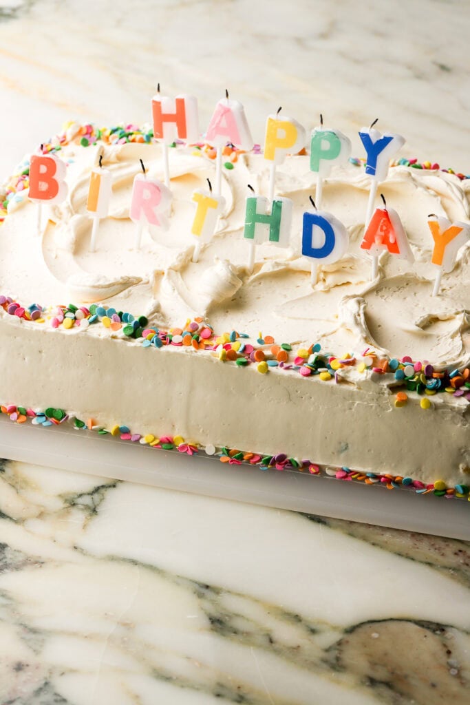 cake fully frosted and decorated with 'happy birthday' rainbow candles and confetti sprinkles
