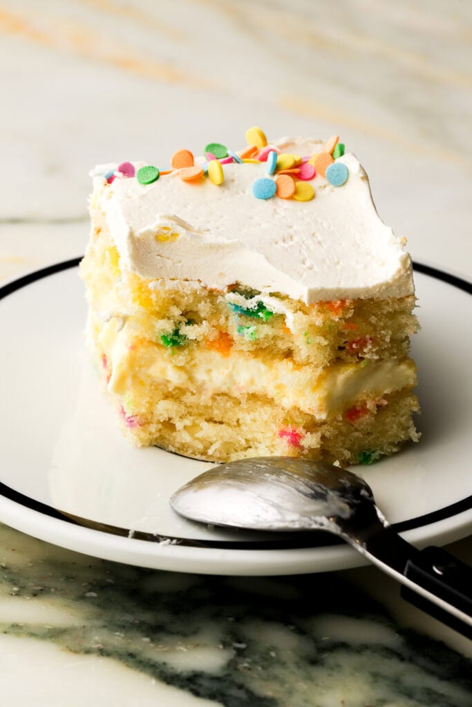 slice of birthday cake on a plate with a bite taken out and the spoon on the edge